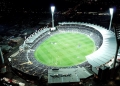 A green sports oval is lit up with bright lights against a black sky